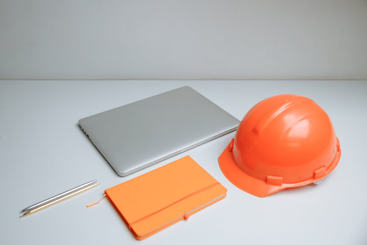 Sleek desk setup featuring a laptop, notebook, and orange hardhat.