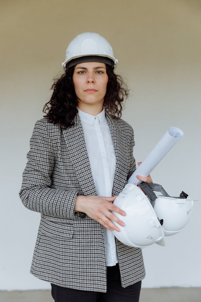 Female architect in safety gear holding blueprints, showcasing professionalism.